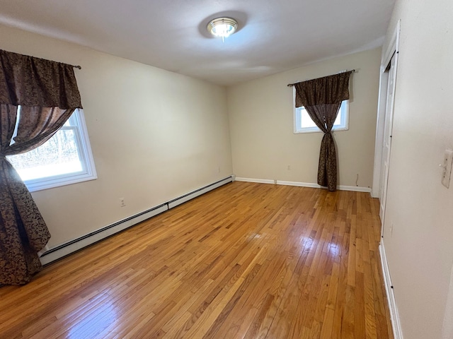 unfurnished bedroom with a baseboard heating unit, multiple windows, baseboards, and light wood-style floors