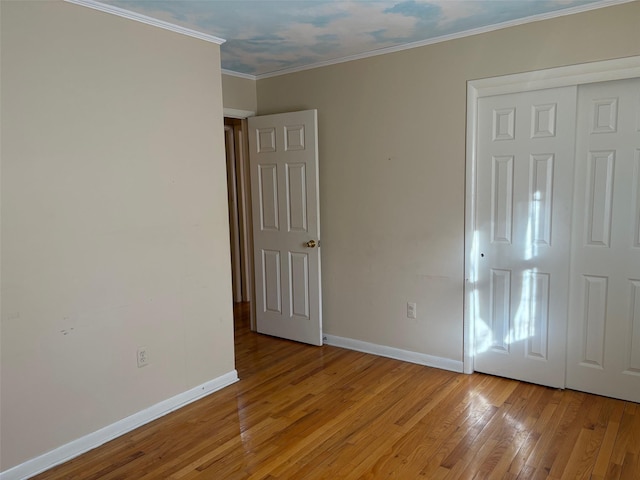 unfurnished bedroom featuring light wood-type flooring, a closet, crown molding, and baseboards