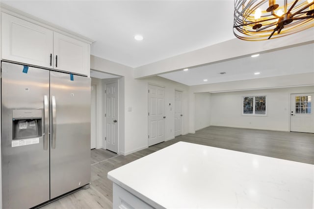 kitchen with stainless steel refrigerator with ice dispenser, an inviting chandelier, light hardwood / wood-style floors, and white cabinets