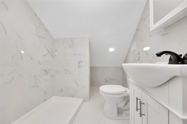 bathroom featuring a tile shower, lofted ceiling, tile walls, vanity, and toilet