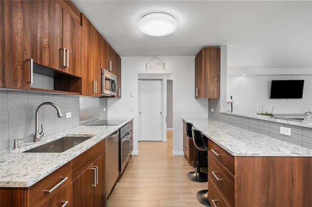 kitchen featuring appliances with stainless steel finishes, sink, light stone counters, and light wood-type flooring