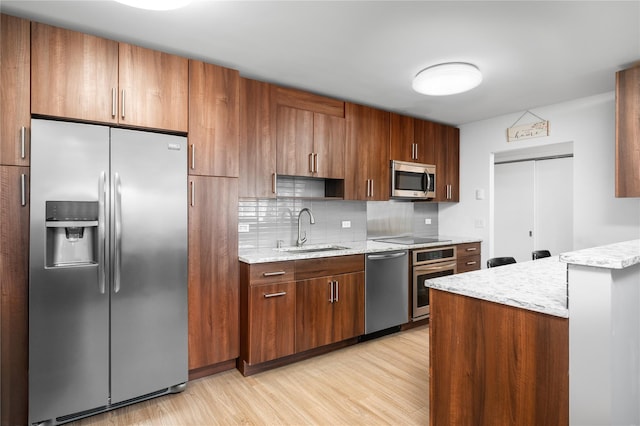 kitchen with sink, stainless steel appliances, tasteful backsplash, light stone counters, and light wood-type flooring