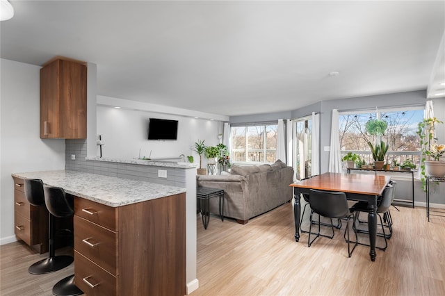 kitchen featuring light stone counters, a kitchen breakfast bar, decorative backsplash, and light wood-type flooring