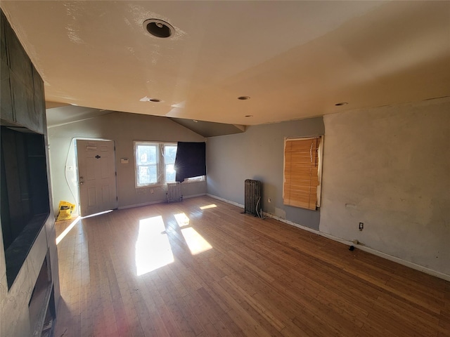 interior space featuring wood-type flooring, vaulted ceiling, and radiator