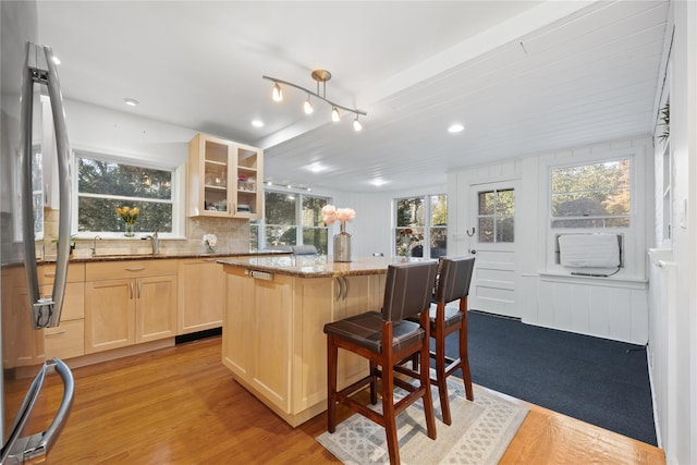 kitchen with a kitchen island, stainless steel refrigerator, a breakfast bar area, dark stone counters, and light brown cabinets