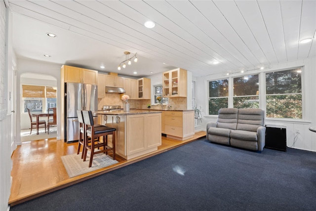 kitchen featuring light brown cabinetry, stainless steel refrigerator, backsplash, a kitchen bar, and a center island