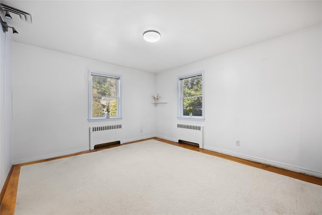 spare room with radiator heating unit, wood-type flooring, and plenty of natural light