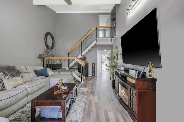 living room featuring beam ceiling, light hardwood / wood-style floors, and a high ceiling