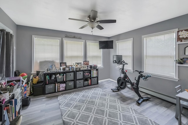 exercise room featuring a baseboard radiator, ceiling fan, and light wood-type flooring