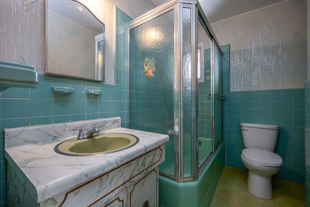 full bathroom with shower / bath combination with glass door, vanity, toilet, and tile walls