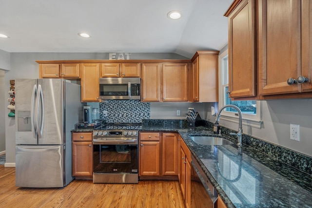 kitchen featuring sink, stainless steel appliances, light hardwood / wood-style floors, decorative backsplash, and dark stone counters