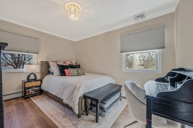 bedroom featuring ornamental molding, hardwood / wood-style floors, and baseboard heating