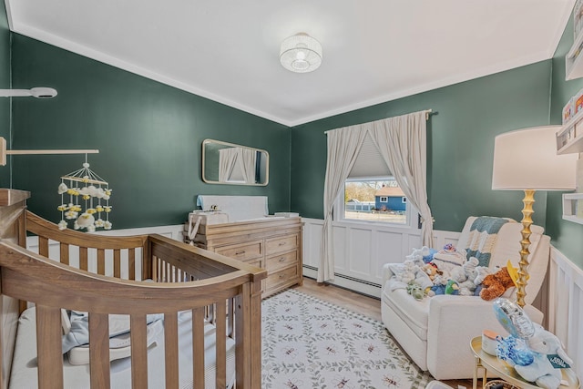 bedroom with crown molding, a nursery area, a baseboard heating unit, and light wood-type flooring