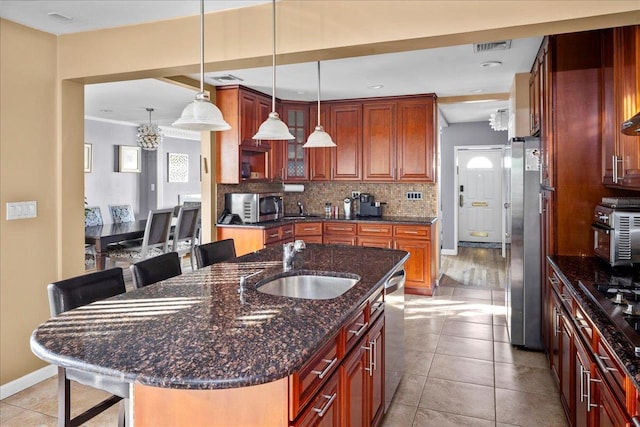 kitchen with a breakfast bar area, appliances with stainless steel finishes, decorative backsplash, a center island with sink, and decorative light fixtures