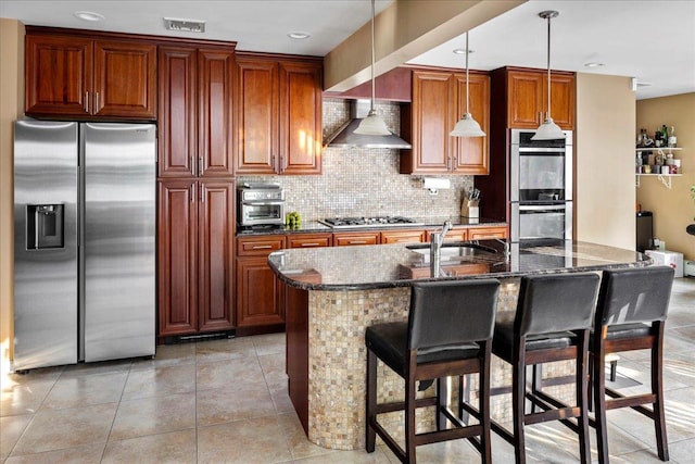 kitchen with wall chimney exhaust hood, sink, a breakfast bar area, hanging light fixtures, and appliances with stainless steel finishes