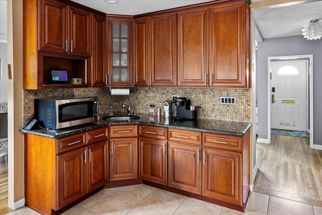 kitchen with sink, decorative backsplash, dark stone counters, and light tile patterned floors