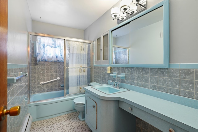 full bathroom featuring toilet, combined bath / shower with glass door, tile walls, baseboard heating, and vanity