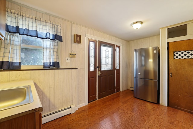 kitchen featuring wooden walls, stainless steel refrigerator, wood-type flooring, sink, and baseboard heating