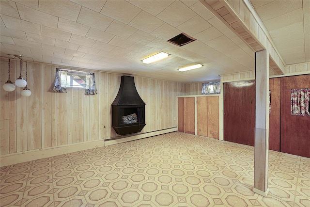 basement featuring a wood stove, wooden walls, and baseboard heating