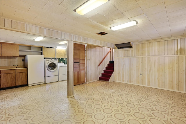 basement with washing machine and dryer, white fridge, and wood walls