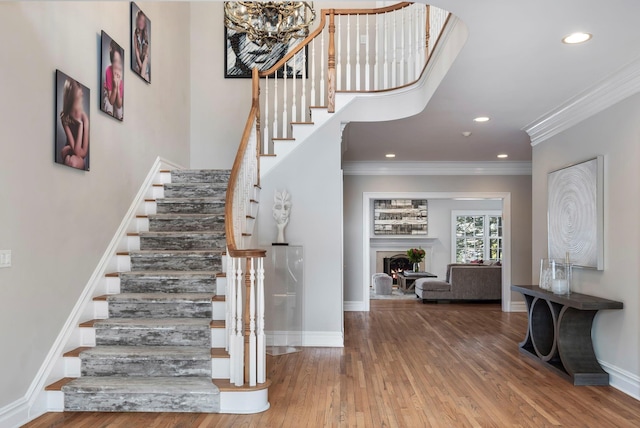 staircase featuring baseboards, ornamental molding, wood finished floors, a lit fireplace, and recessed lighting