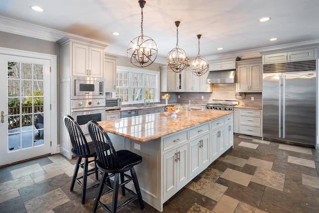 kitchen with built in appliances, ventilation hood, an island with sink, a kitchen bar, and pendant lighting