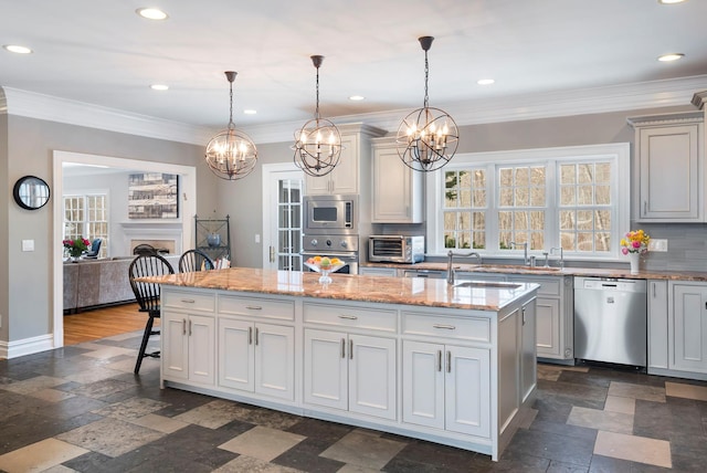 kitchen with appliances with stainless steel finishes, a kitchen island with sink, hanging light fixtures, and light stone countertops