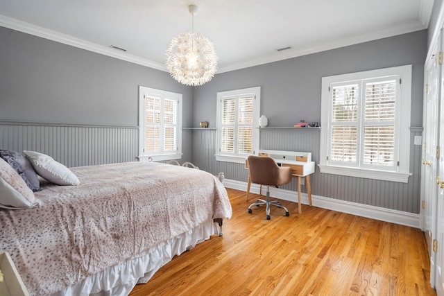 bedroom featuring a wainscoted wall, multiple windows, visible vents, and wood finished floors