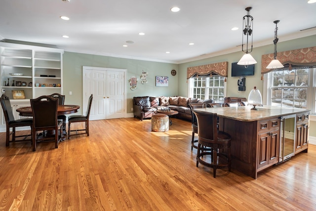 kitchen featuring a center island, wine cooler, decorative light fixtures, light wood-style flooring, and light stone countertops