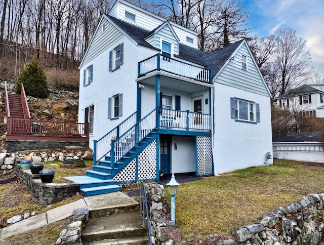 view of front of home featuring roof with shingles, stucco siding, a balcony, a front lawn, and stairs