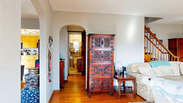 living area with wood finished floors, baseboards, a ceiling fan, arched walkways, and stairs