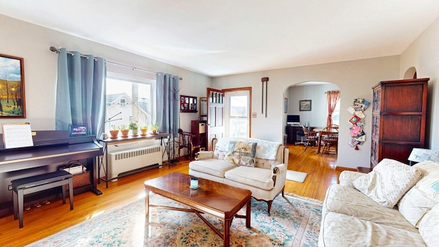 living area with arched walkways, wood finished floors, and radiator heating unit