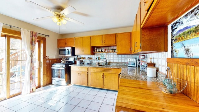 kitchen with brown cabinets, a ceiling fan, a sink, backsplash, and stainless steel appliances