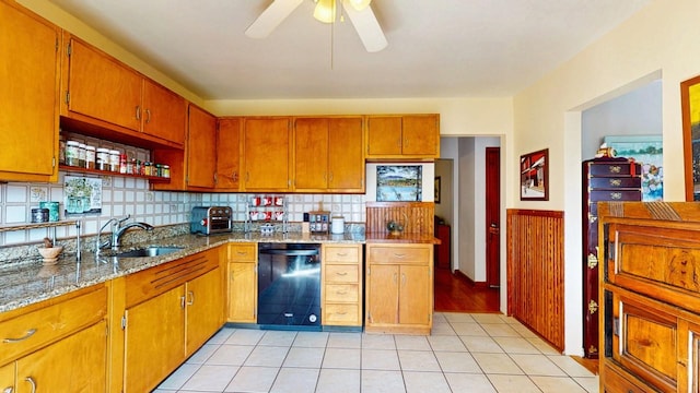 kitchen featuring light tile patterned floors, light stone countertops, brown cabinetry, a sink, and black dishwasher