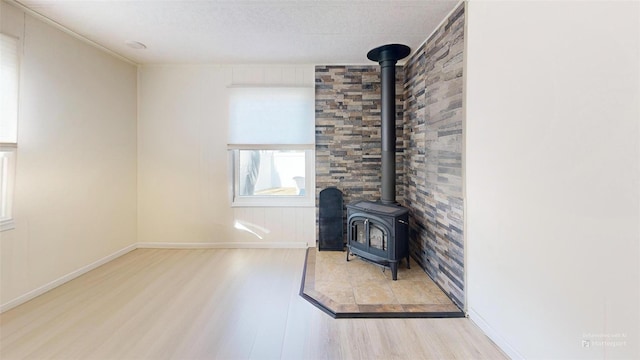 unfurnished living room featuring a wood stove, baseboards, and wood finished floors