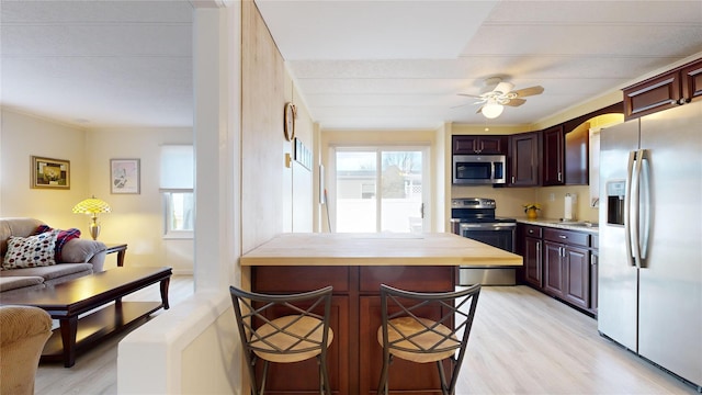 kitchen with light wood-type flooring, stainless steel appliances, a breakfast bar area, and a ceiling fan