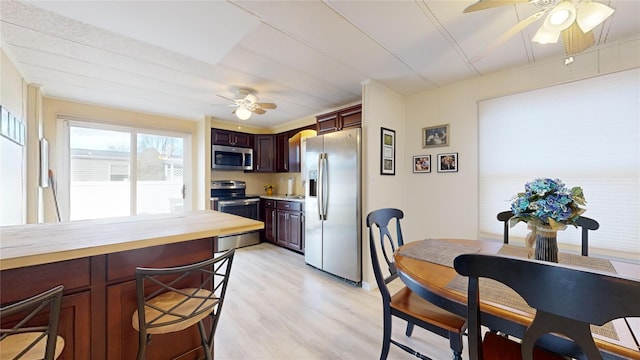 kitchen featuring ceiling fan, butcher block countertops, a breakfast bar area, appliances with stainless steel finishes, and light wood-style floors