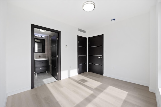 unfurnished bedroom featuring sink, light wood-type flooring, and ensuite bath