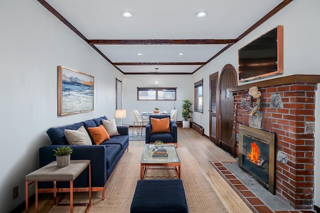 living room featuring crown molding, beam ceiling, hardwood / wood-style floors, and a brick fireplace