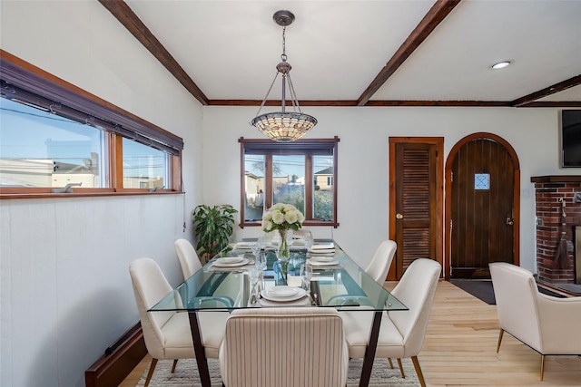 dining space featuring a brick fireplace, beam ceiling, and light wood-type flooring