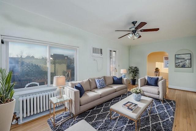 living room with ceiling fan, radiator heating unit, wood-type flooring, and a wall unit AC