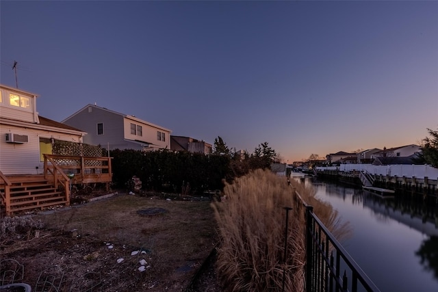 yard at dusk featuring a deck with water view and a wall mounted AC