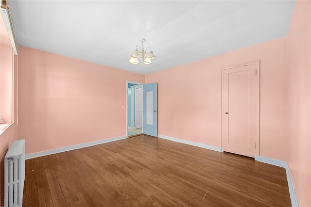 empty room with radiator, hardwood / wood-style flooring, and a notable chandelier