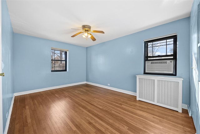 unfurnished room featuring ceiling fan, radiator heating unit, light wood-type flooring, and cooling unit