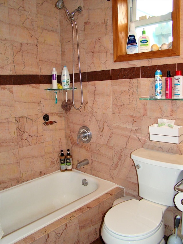 bathroom featuring tiled shower / bath, toilet, and tile walls