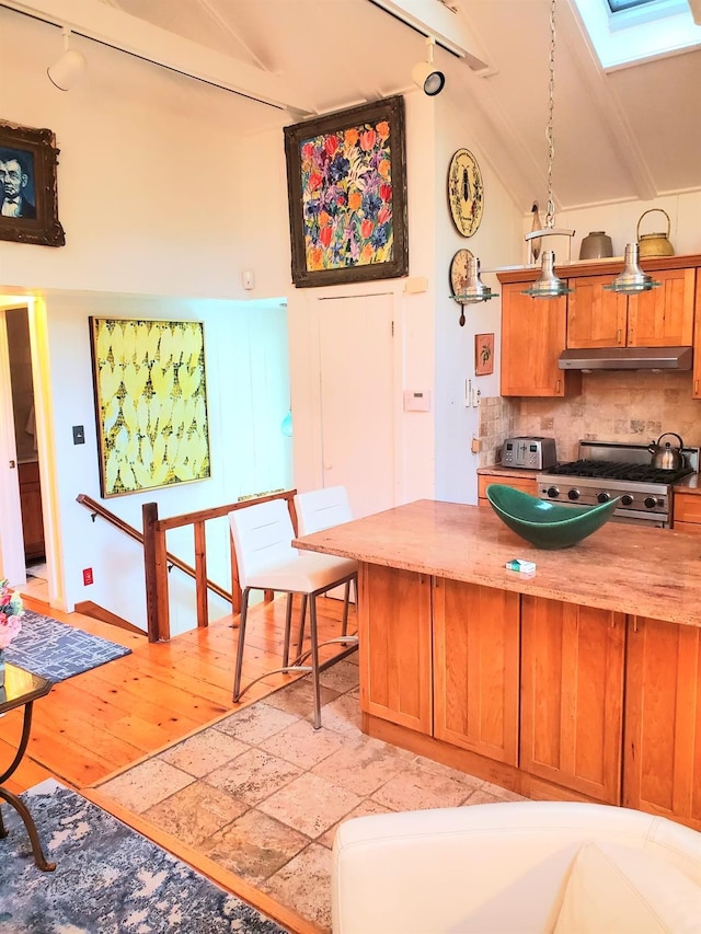 kitchen with backsplash, light hardwood / wood-style flooring, lofted ceiling with skylight, and stainless steel range oven