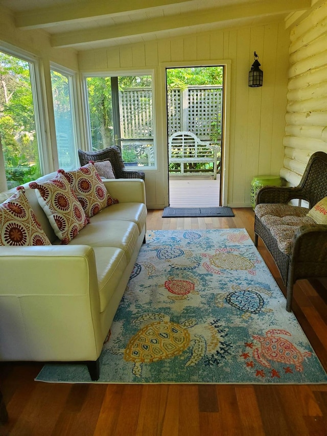 living room with beamed ceiling, a healthy amount of sunlight, wood-type flooring, and rustic walls