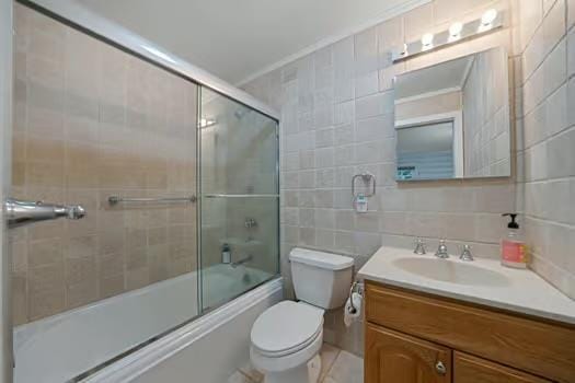 full bathroom with combined bath / shower with glass door, tile walls, backsplash, vanity, and toilet