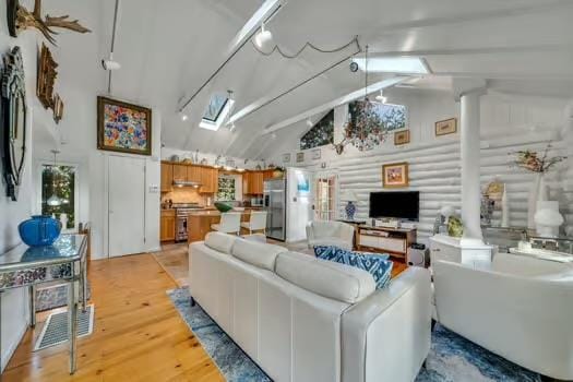 living room featuring high vaulted ceiling, a skylight, beamed ceiling, log walls, and light hardwood / wood-style flooring