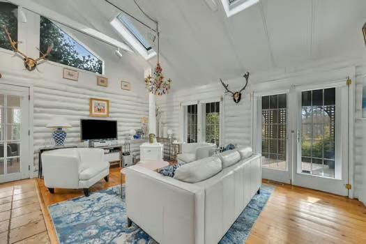 living room with log walls, a skylight, high vaulted ceiling, and light wood-type flooring